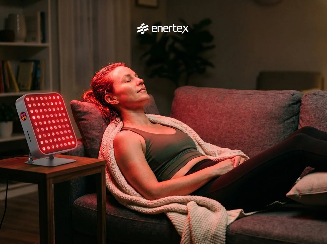 Una mujer relajada con los ojos cerrados en un sofá, recibiendo una sesión de terapia de luz roja de un panel de Envertex en un salón acogedor
