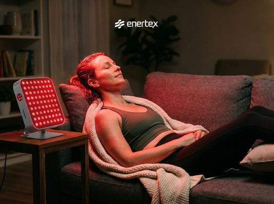 Una mujer relajada con los ojos cerrados en un sofá, recibiendo una sesión de terapia de luz roja de un panel de Envertex en un salón acogedor